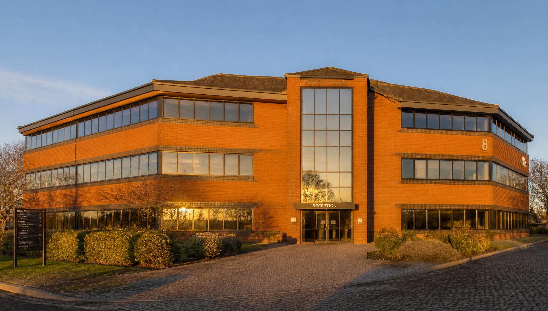 Golden-hour view of a detached three-storey 1990s brick office building with ribbon glazing